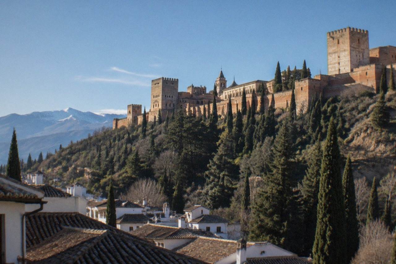 The Alhambra palace complex on its hill above the red rooftops of Granada with mountains in the background
