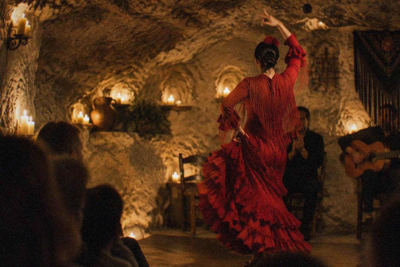 A flamenco dancer in a red dress performing inside a candle-lit cave venue in Granada