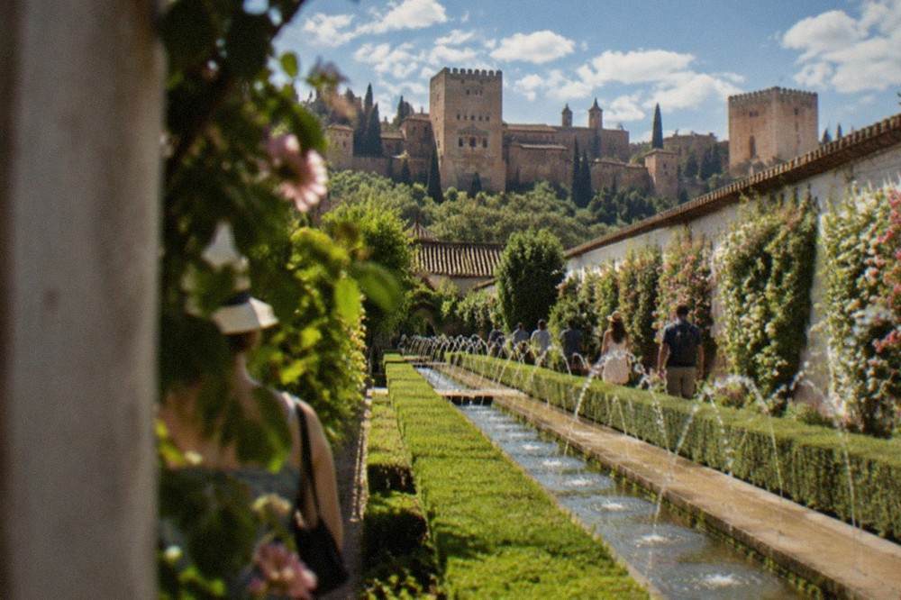 Visitors walking through the irrigated gardens of the Generalife with the Alhambra walls behind
