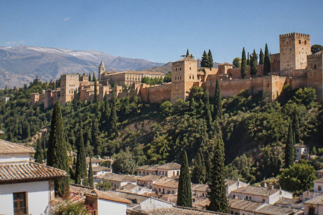 The Alhambra palace complex seen across a red-tiled city skyline with mountains behind