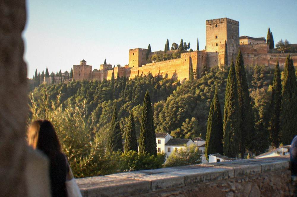 A stone viewpoint terrace with the Alhambra palace walls rising on the opposite hillside