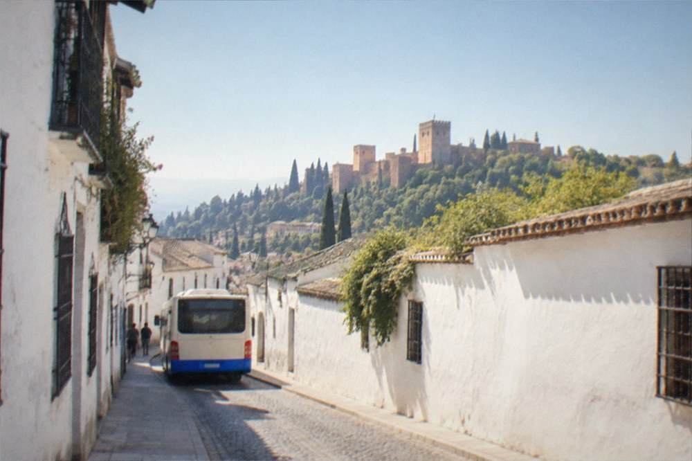 A city bus on a narrow street at the edge of a hillside old quarter