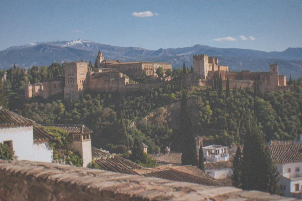 View from a hilltop plaza across rooftops to the Alhambra and mountains beyond