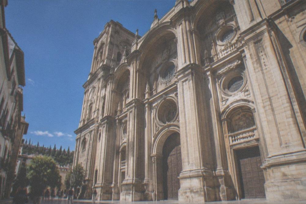 Visitors walking beside the ornate stone facade of Granada Cathedral near the edge of the Realejo
