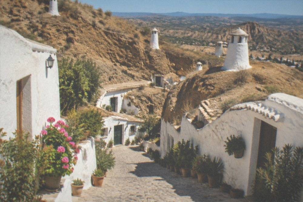 A steep cobbled lane between white cave houses with potted plants along the walls