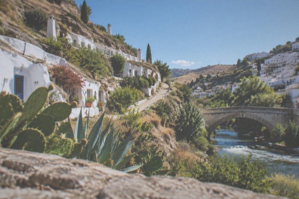 A stone bridge over a river with hillside houses above on both sides