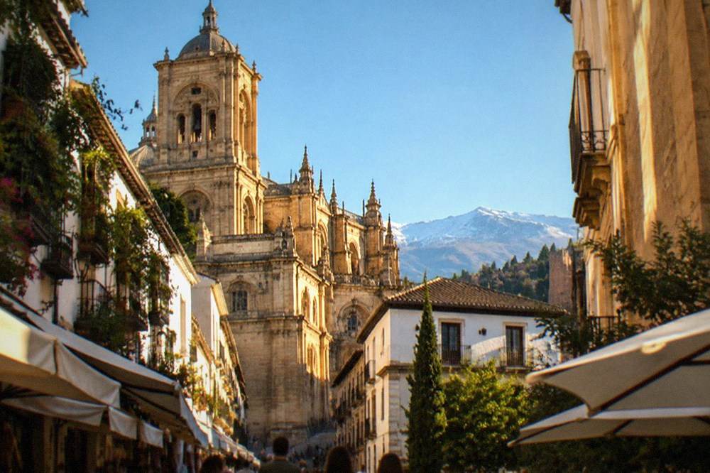 A pedestrian street in central Granada with the Cathedral rising behind low shop awnings