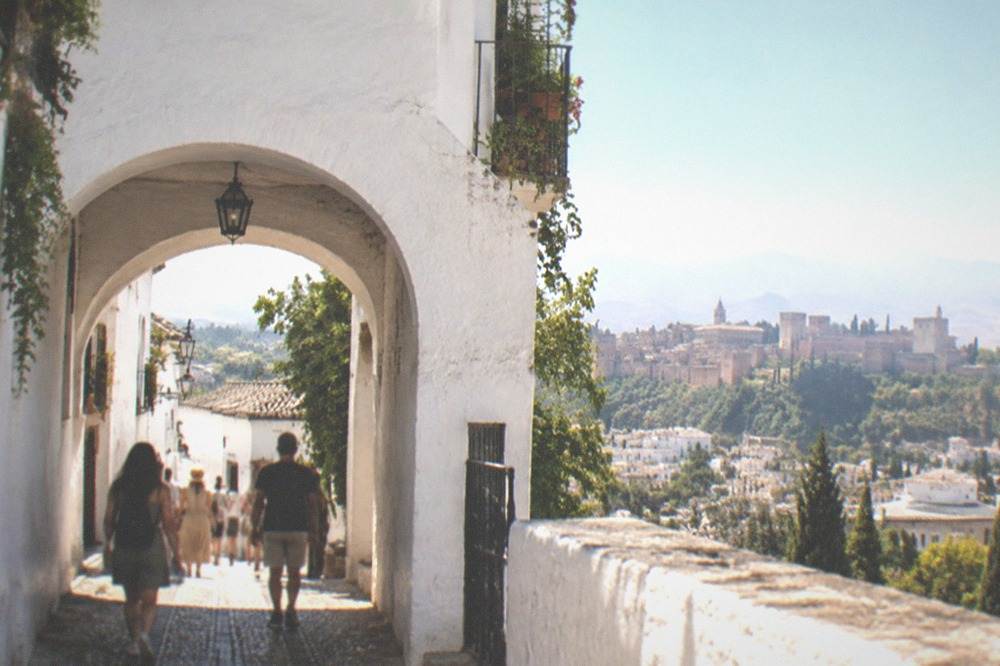 Visitors walking through a narrow arch in a whitewashed shopping arcade in Granada