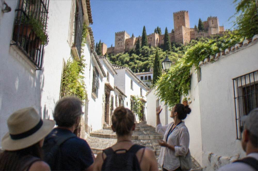 A guide speaking to a small group of visitors in a sunlit square in the Albaicin district