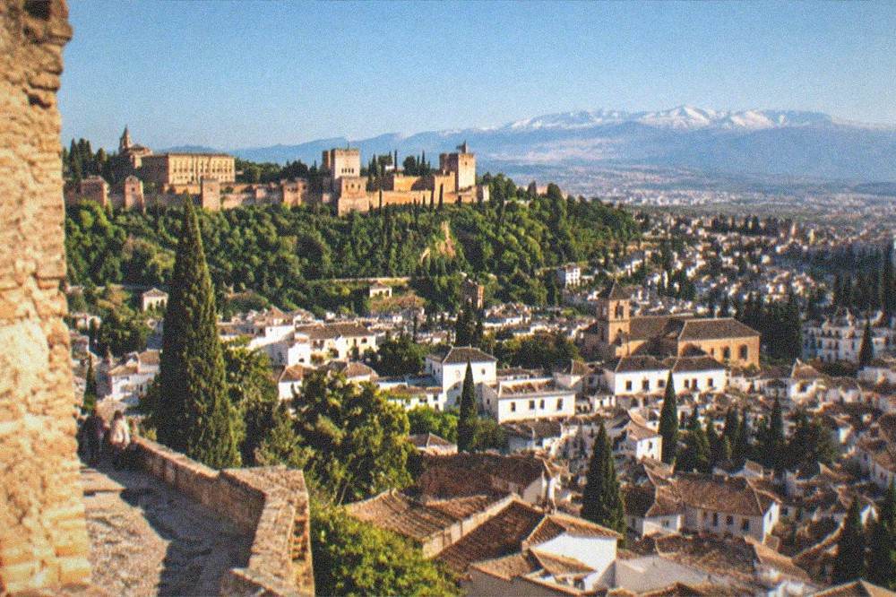 Evening view across Granada rooftops from a fortress tower with the Sierra Nevada on the horizon