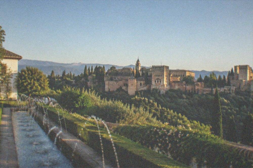 A view across a green ravine toward the Alhambra's towers from the upper Generalife gardens