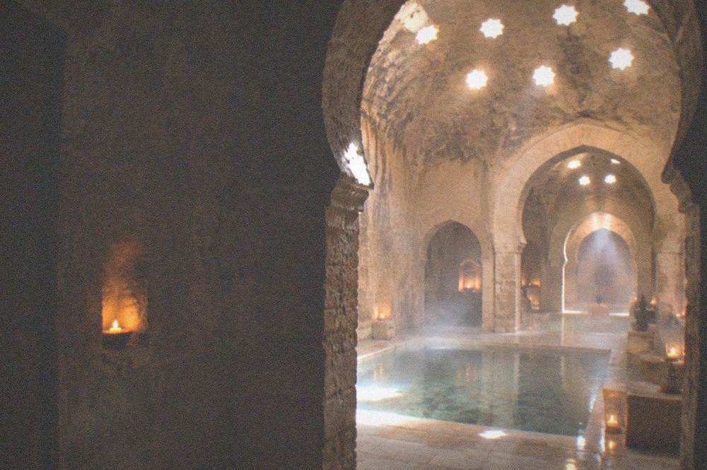 Stone doorway opening onto a candlelit bathing hall with arched ceilings