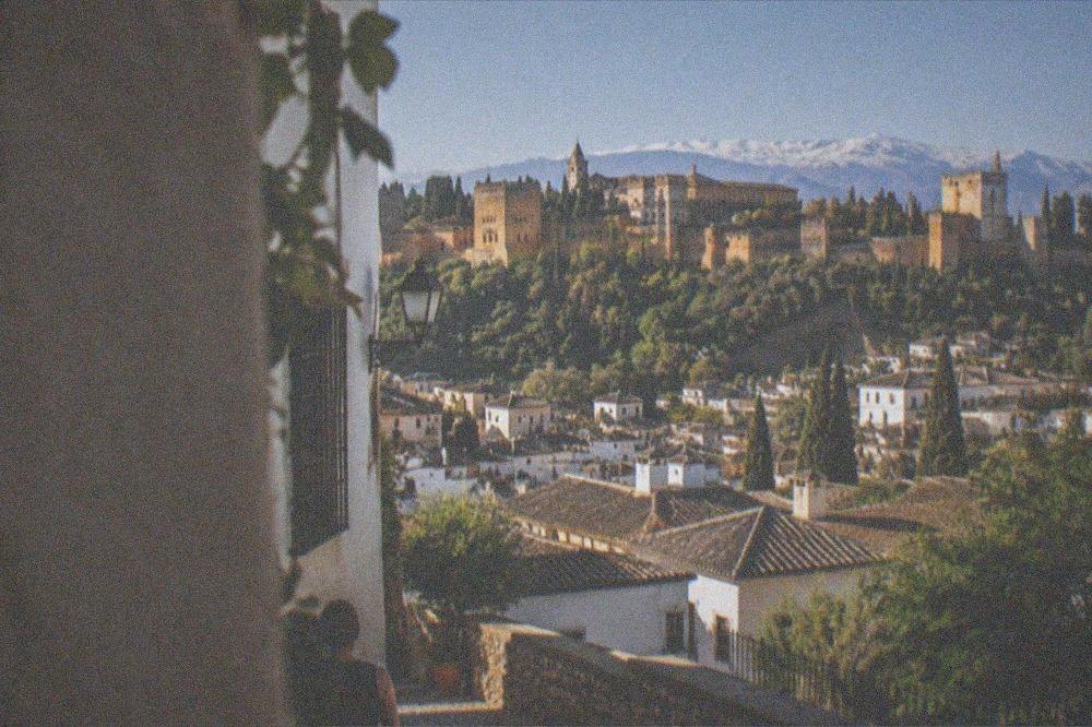 Evening view from a hillside terrace across the lit rooftops of old Granada toward a floodlit palace hill