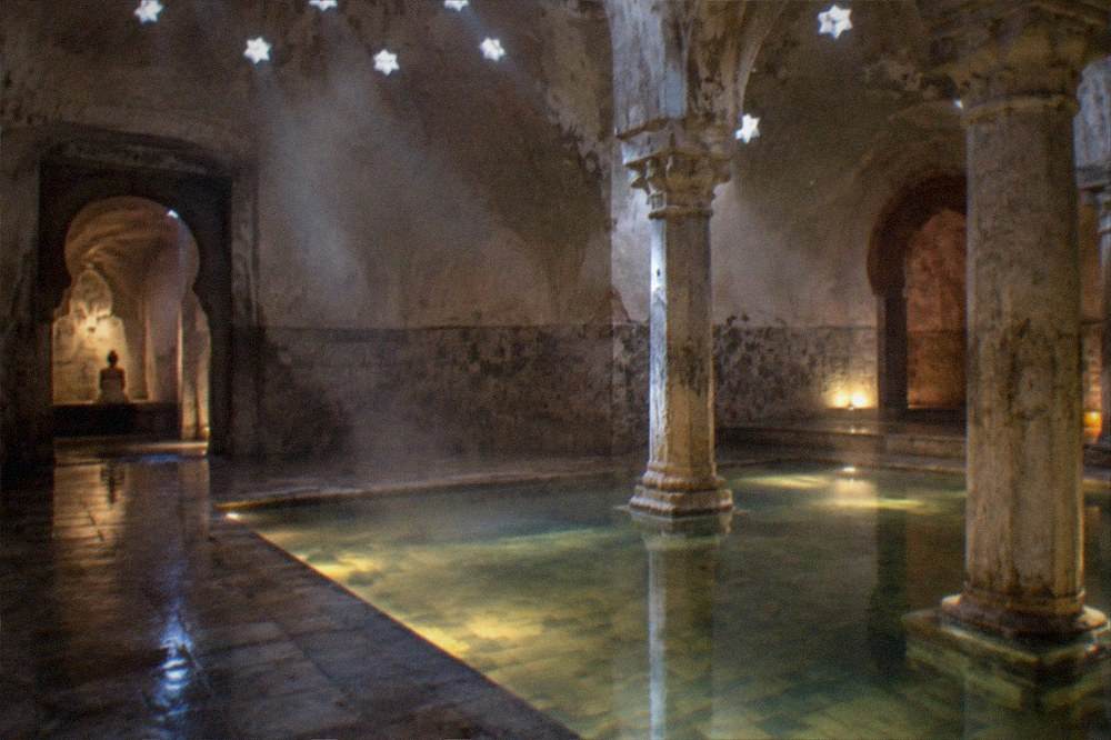 Shallow warm pool with underwater lighting and stone columns reflected in still water