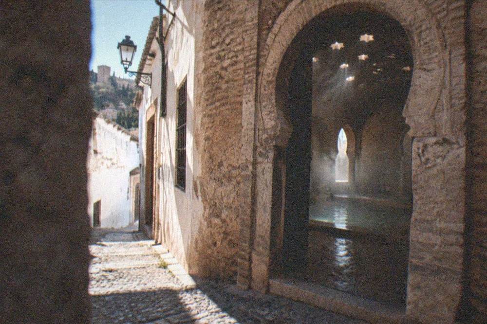 Arched stone doorway of a bathhouse seen from a narrow evening street in old Granada