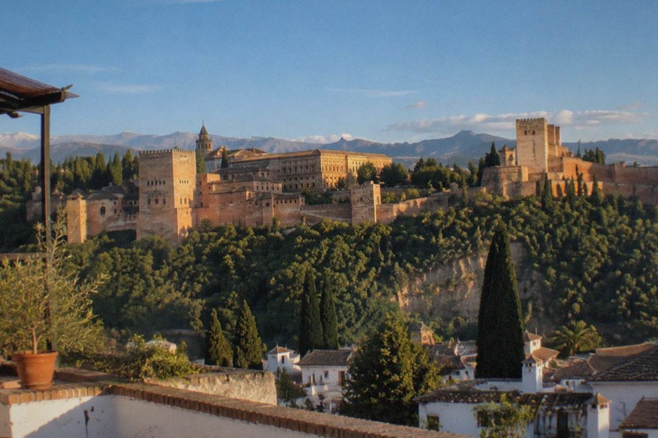 Viewpoint terrace in Granada at sunset with the Alhambra palace on a hill opposite and mountains in the distance