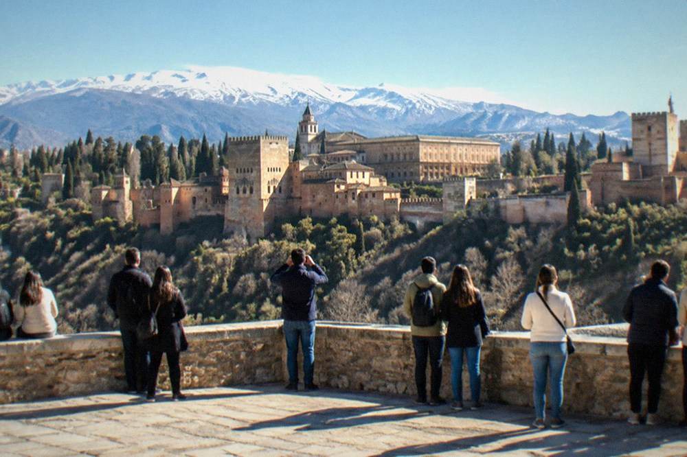 Crowd of people gathered at a stone viewpoint wall watching the sun set over a palace