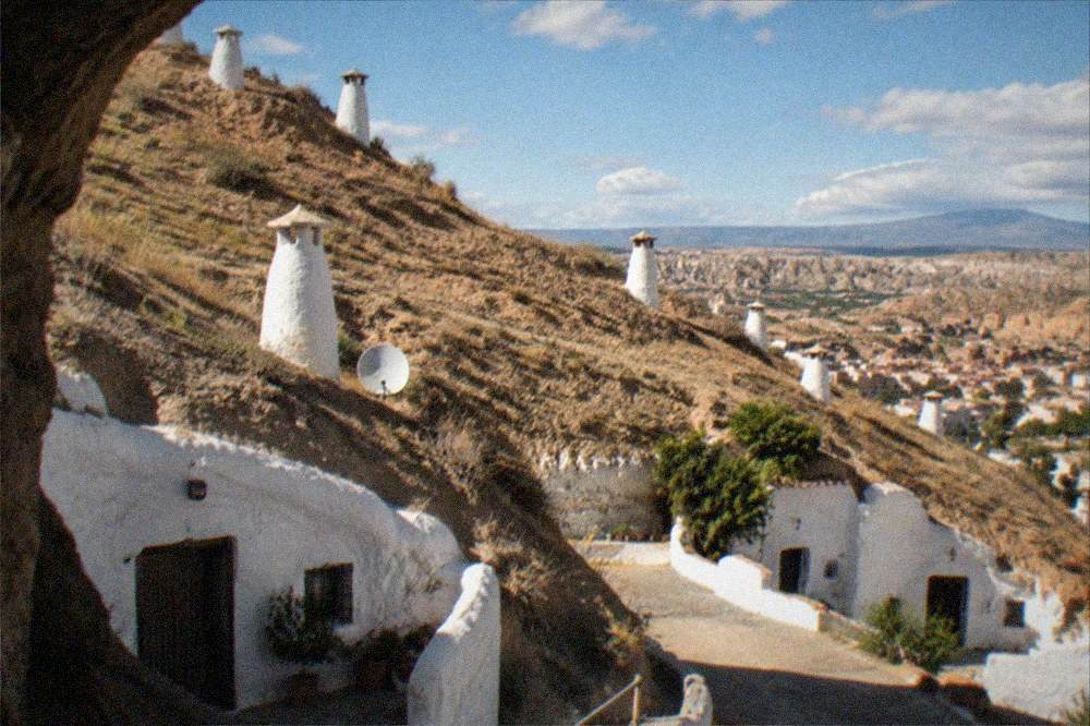 Whitewashed cave house doors carved into a hillside above a city at dusk