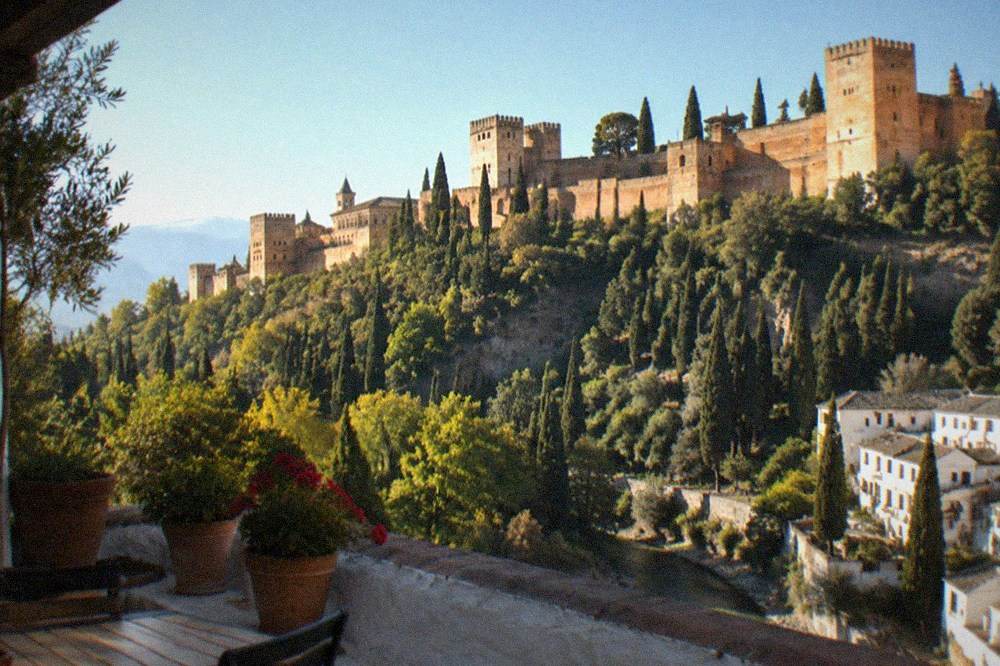 A hillside terrace with potted plants and a wide view across to the Alhambra and the Darro valley