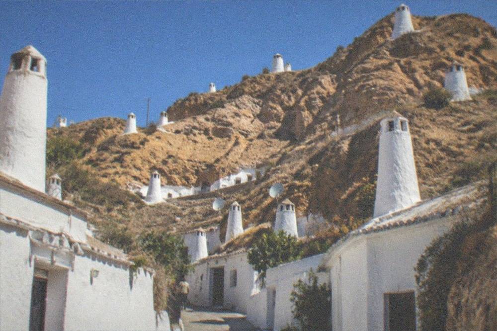 A narrow lane of cave house facades with chimneys and whitewashed fronts on the Sacromonte hillside