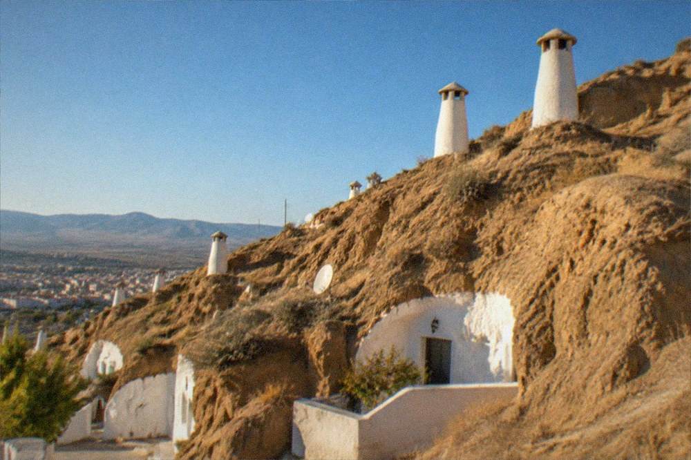 Cave house chimneys rising from the hillside slope with the city of Granada below