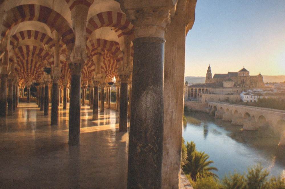 The Roman bridge and city walls of Cordoba reflected in the Guadalquivir river at golden hour