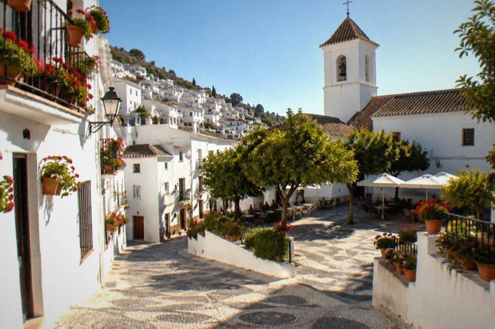 A village square with a church tower and outdoor tables under shade