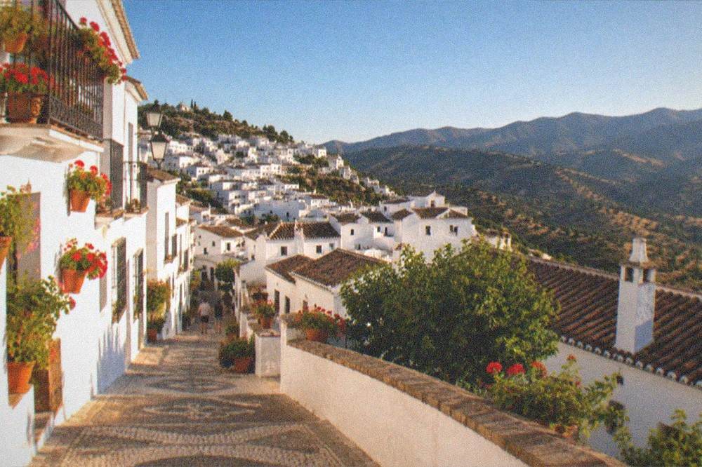 An evening view over white village rooftops with warm light on the hills