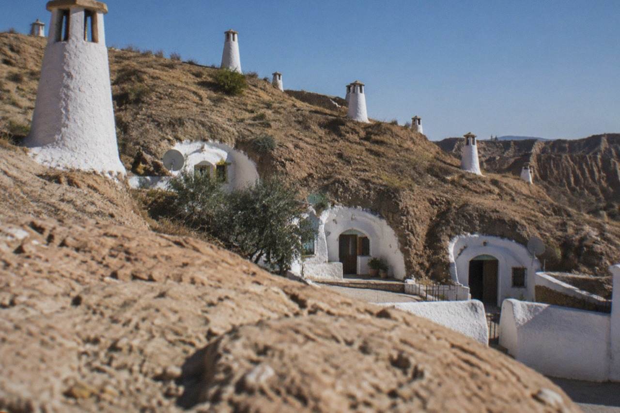 White chimney stacks rising from a hillside of cave house entrances under a blue sky