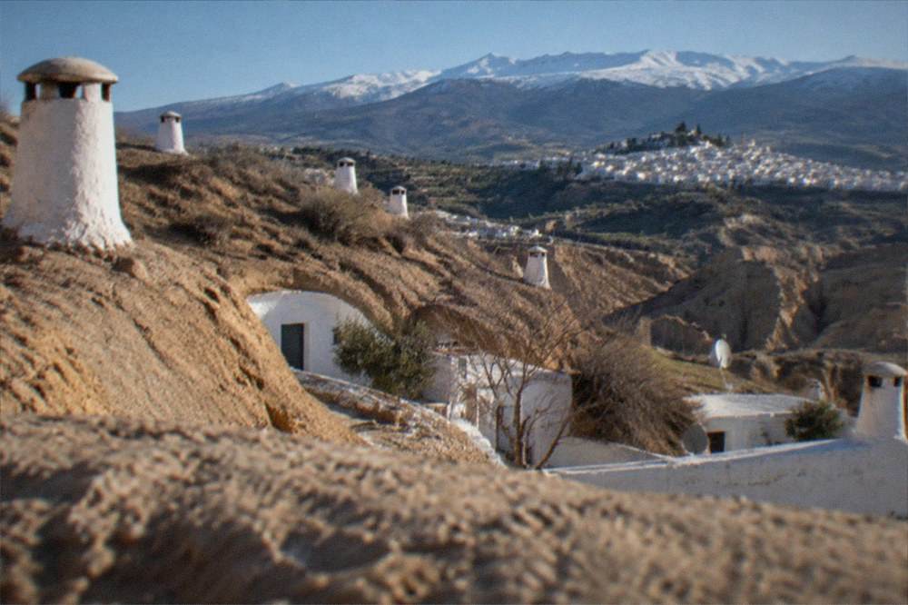 White mountain villages terraced on a green hillside below snowy peaks