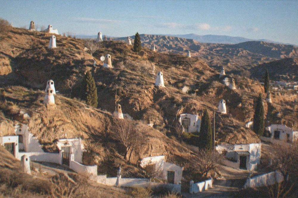 A wide view over a hillside neighbourhood of cave houses under a late evening sky