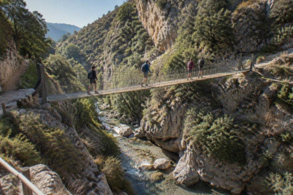 Hikers crossing a hanging bridge over a mountain stream in a narrow canyon