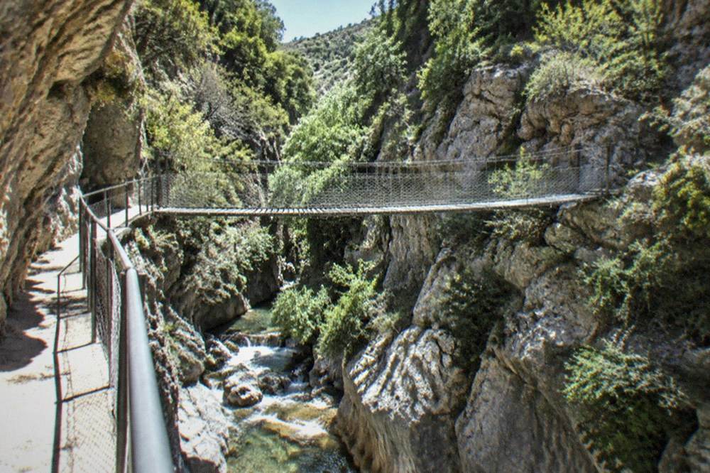 A walkway cut into the cliff face inside a shaded canyon with water below