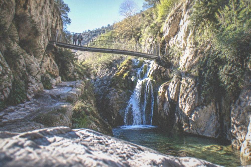 Water falling over rocks into a green pool inside a narrow canyon