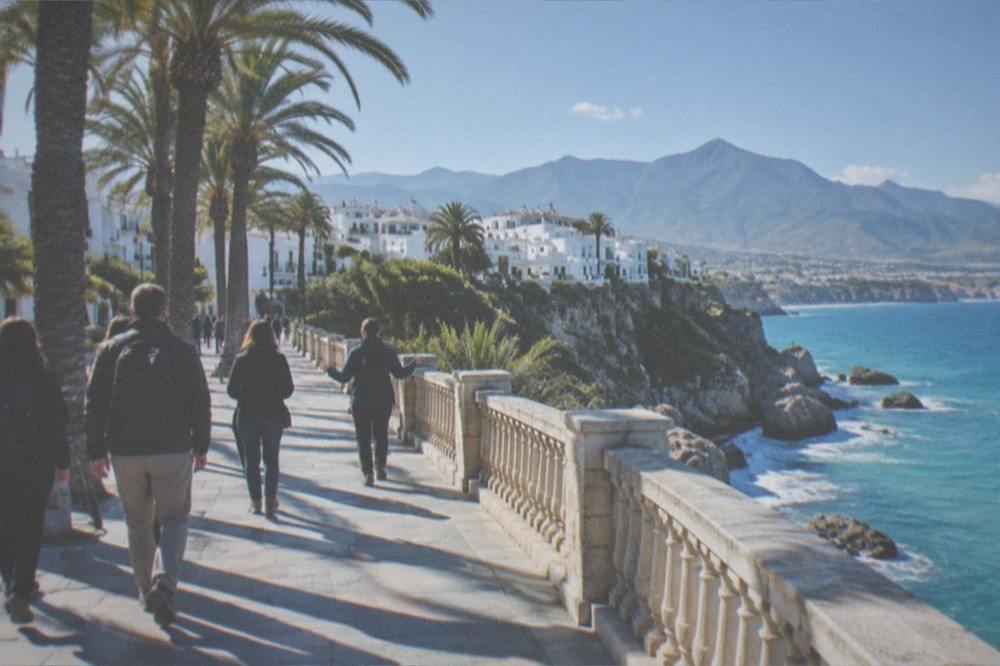Small group of travellers walking with a guide along a seafront street