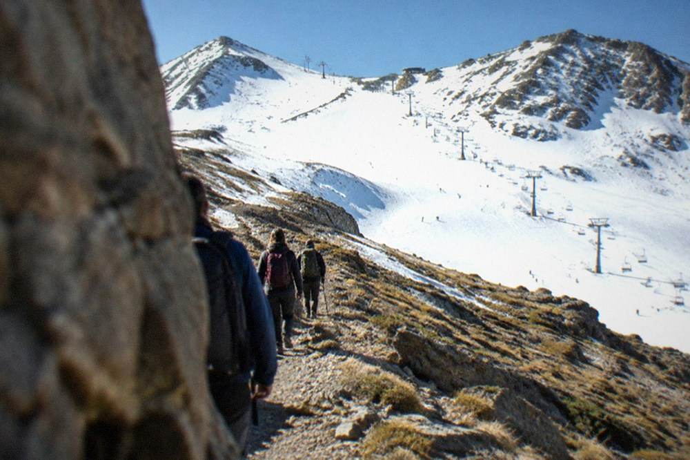 Small group of hikers with backpacks walking a rocky ridge path above the tree line