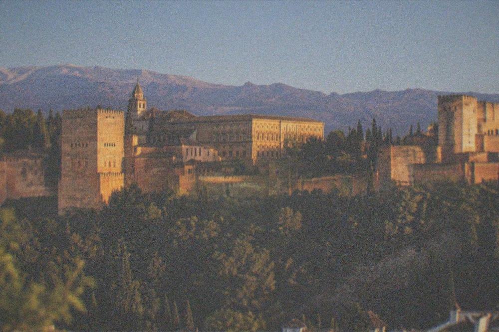 Evening view of the Alhambra palace on its hillside with mountains behind at dusk