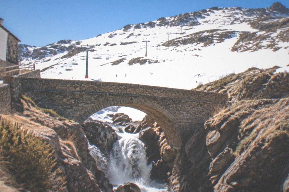 A narrow stone bridge spanning a rocky gorge with a waterfall below