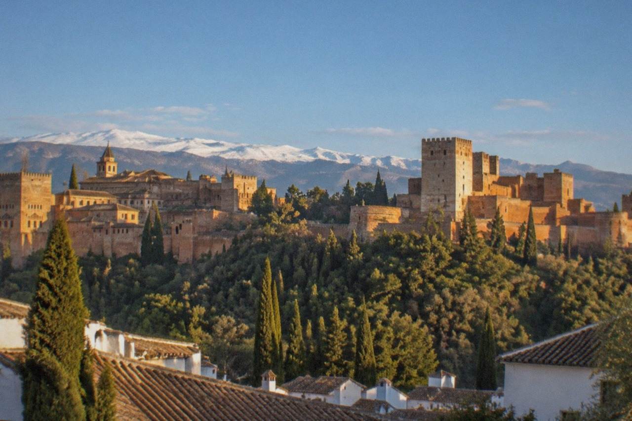 The red walls and towers of the Alhambra rising above Granada with the Sierra Nevada in the background