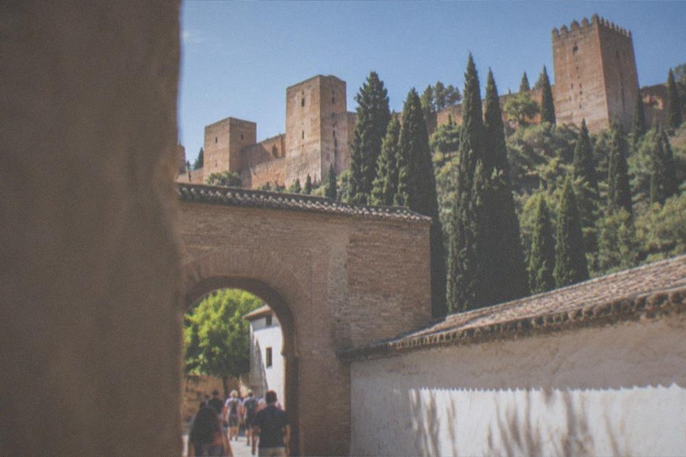 Visitors walking through an arched gateway in the Alhambra complex