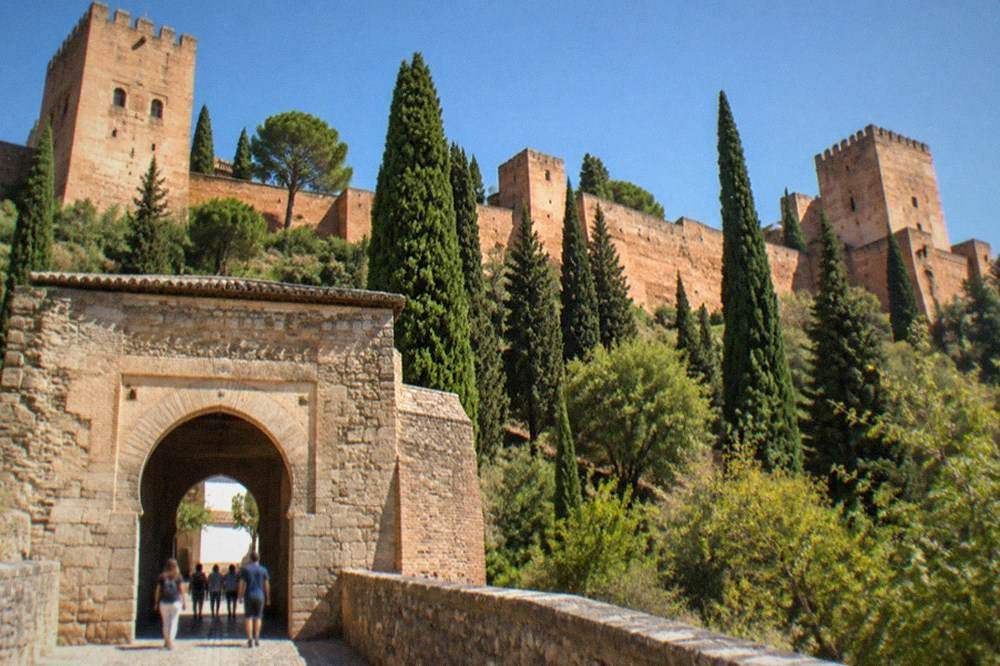 A stone gate of the Alhambra with visitors passing through into the walled complex