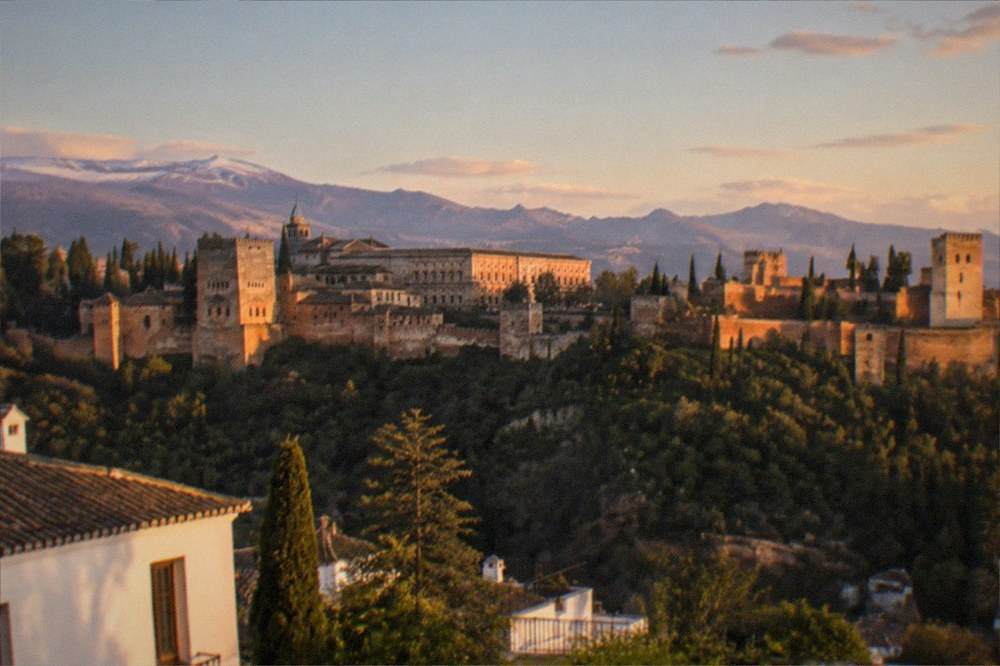 The Alhambra palaces seen from a viewpoint across the valley at sunset, with mountains behind