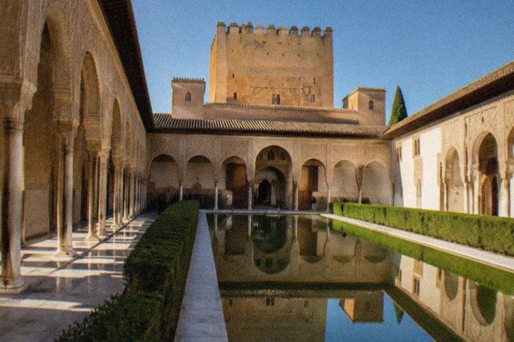 A lit courtyard with a long reflecting pool inside the Nasrid Palaces at night