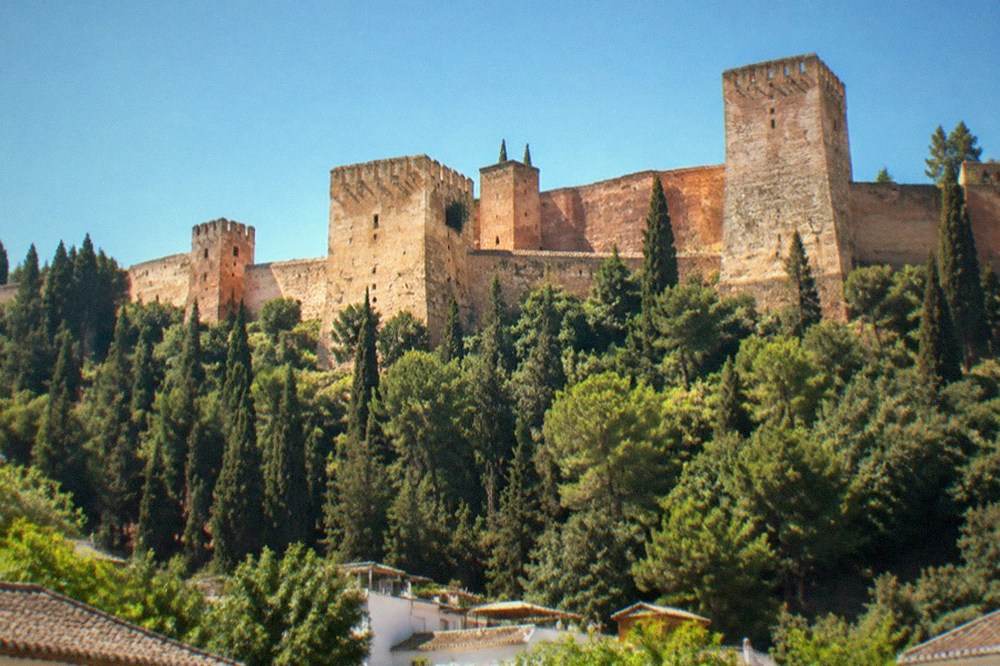 The Alhambra walls and towers lit by floodlights above the dark trees of the hillside