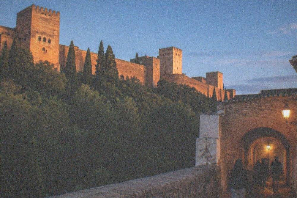 A small group of visitors walking through a lamplit arched passage in the Alhambra at night