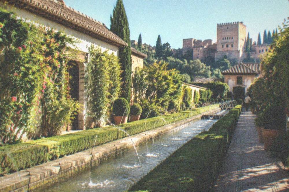 Terraced gardens with clipped hedges and water channels lit softly at night in the Generalife