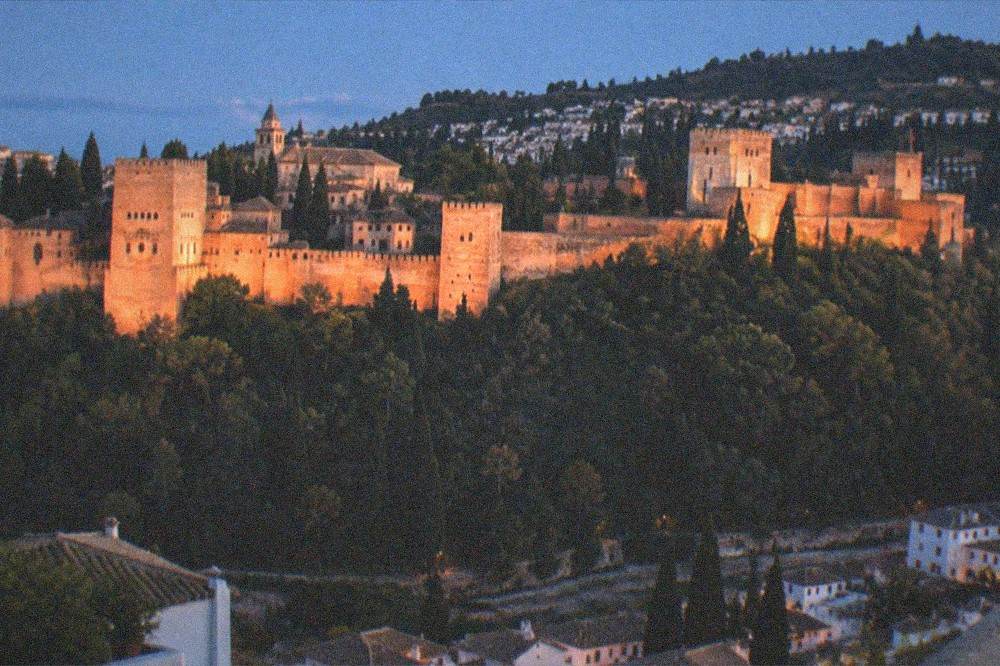 The floodlit Alhambra seen from across the Darro valley with the dark Albaicin hillside behind