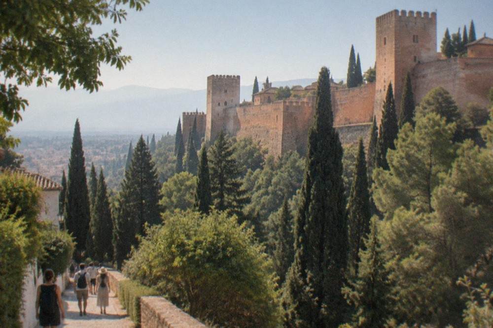 Visitors walking through the tree-lined path toward the Generalife gardens of the Alhambra