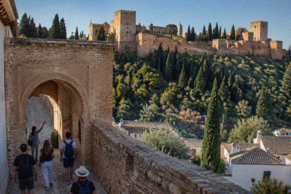 Visitors walking through a horseshoe arch in the Alhambra with a guide pointing at carved decoration