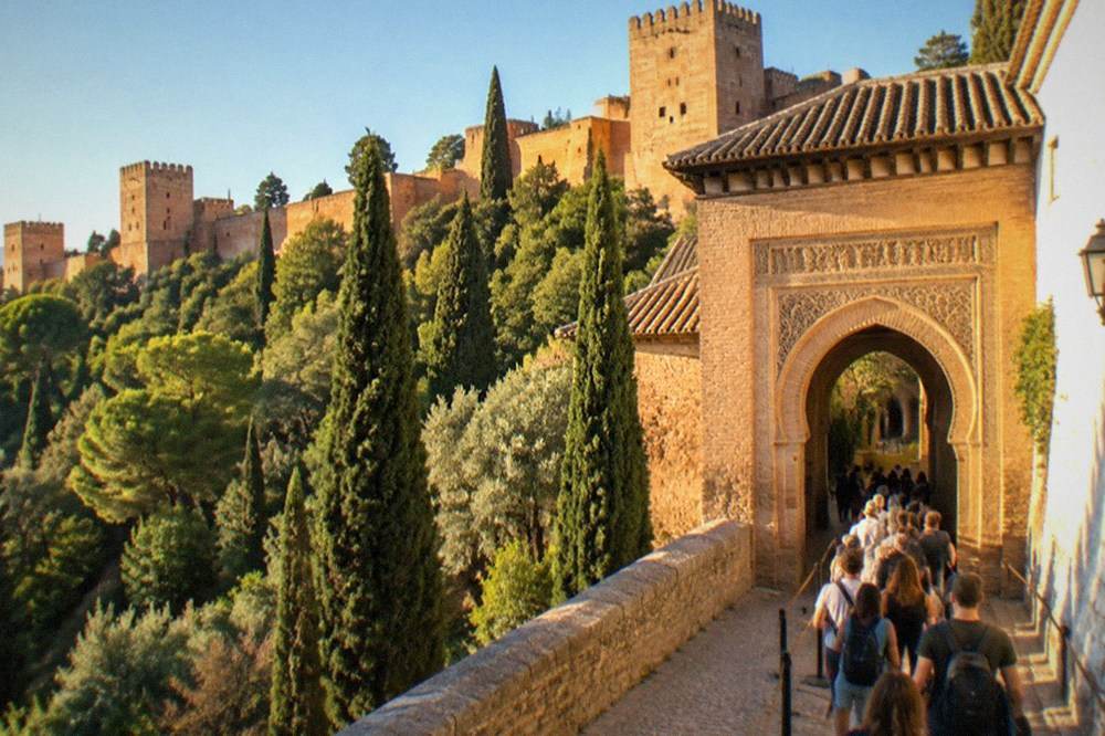 A queue of visitors waiting at an ornate Alhambra gateway in warm afternoon light
